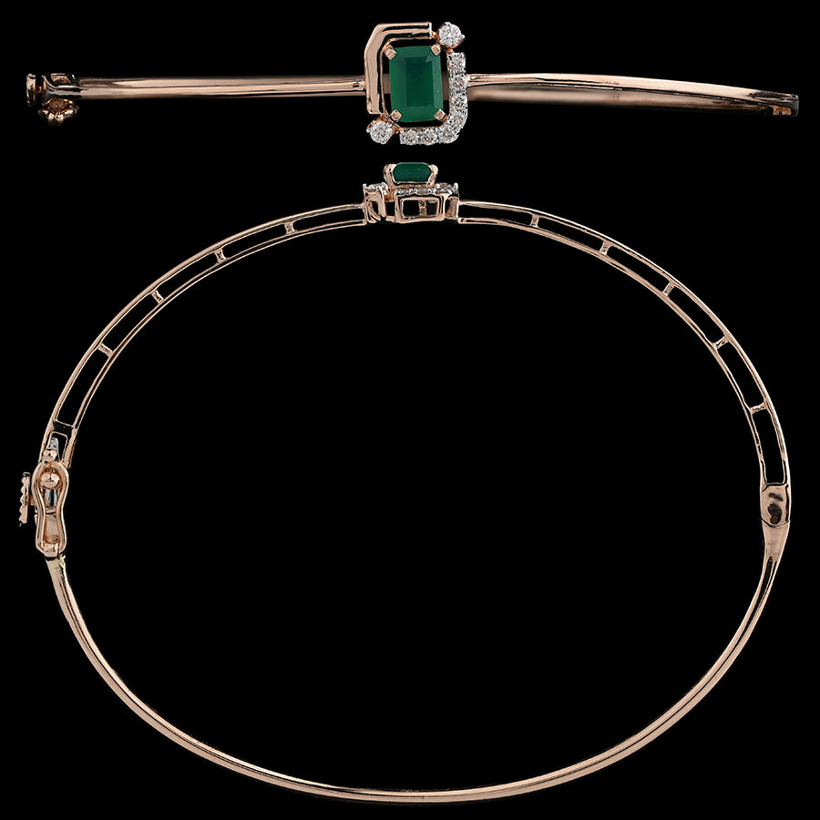 Graceful gold bangle bracelet adorned with a radiant green gemstone centerpiece and sparkling accents, perfect for elegant occasions. A timeless statement of luxury by jnjbymadhuri.