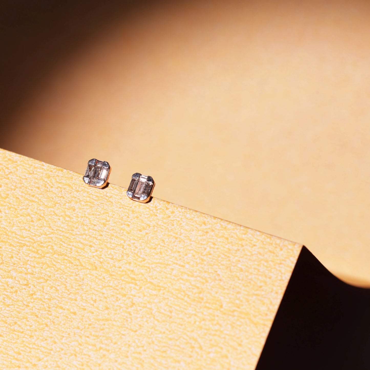 This photo showcases the same jnjbymaduri geometric rectangular stud earrings in a lifestyle setting. The minimal, reflective surface of the design pairs elegantly with the warm backdrop, highlighting their understated luxury—perfect for both daily wear and formal settings.