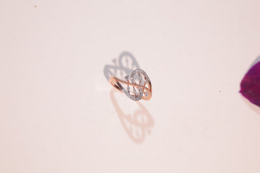 Rose gold ring with a swirling, open design and embedded diamonds, casting an elegant shadow on a pale surface with a purple object in the corner.