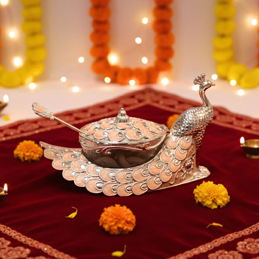 Decorative silver peacock-shaped container on a red fabric background with lights and flowers.