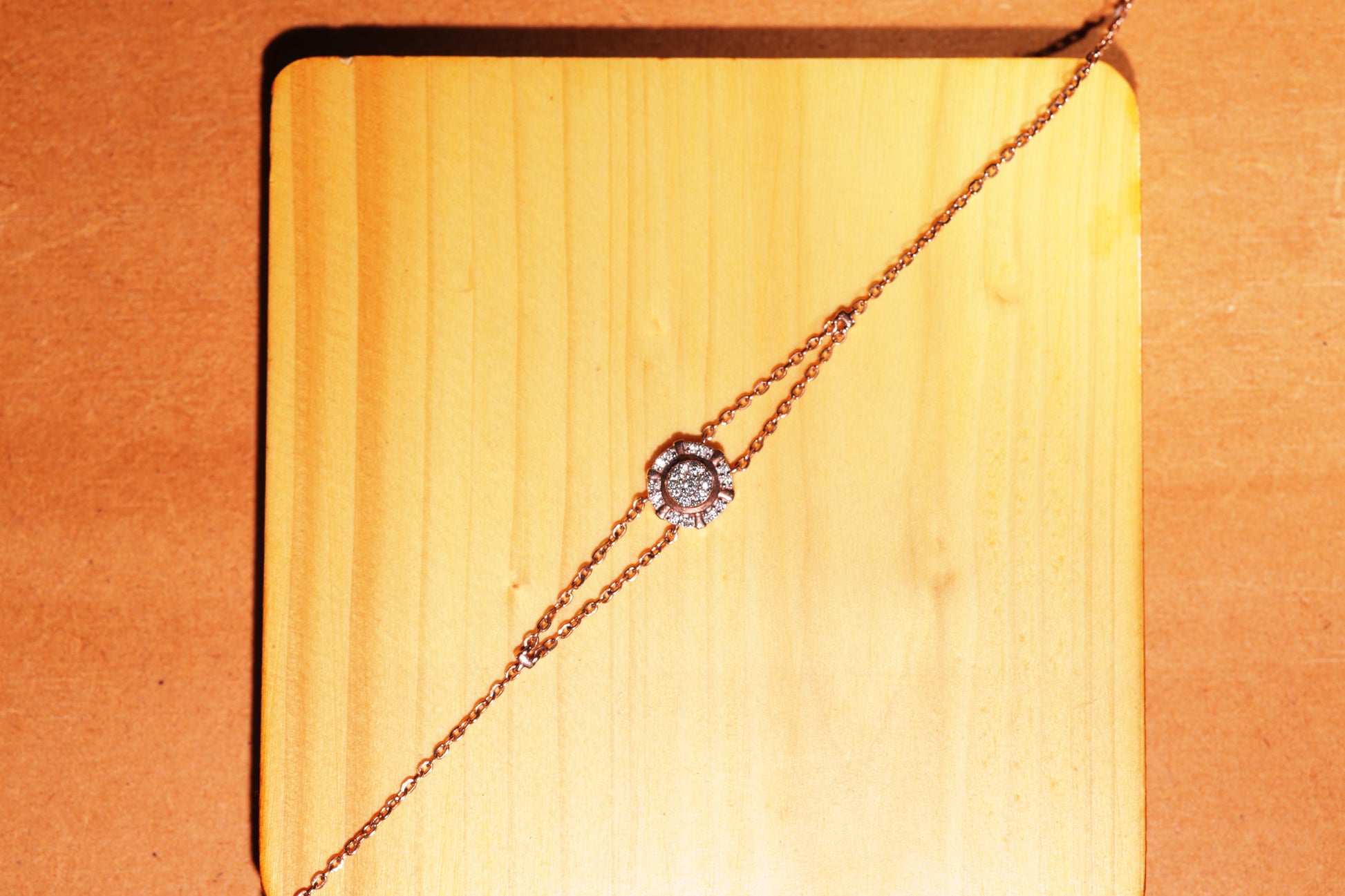 This image features the same rose gold bracelet by jnjbymadhuri, now displayed on a light wooden square base. The floral diamond motif remains the focal point, and the warm wood tones complement the metal’s rose hue, enhancing the bracelet’s elegance with a rustic yet refined presentation.