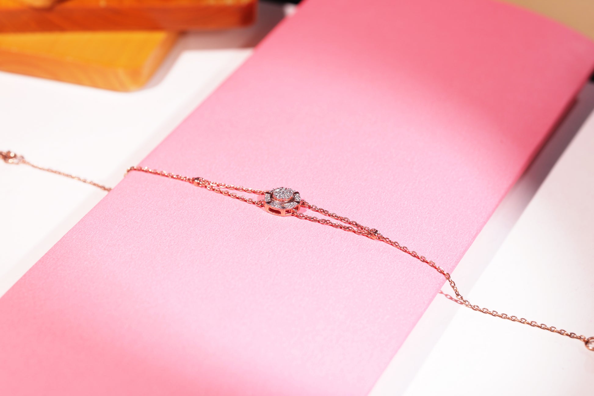 A delicate rose gold bracelet by jnjbymadhuri, showcasing a central diamond-studded floral motif, styled on a soft pink background with warm lighting—perfectly capturing the elegance and sophistication of modern minimalist jewelry.