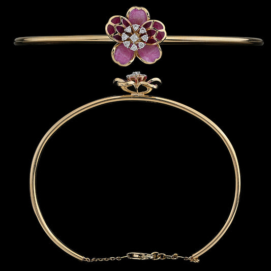 An exquisite gold bangle by jnjbymadhuri, featuring a beautifully crafted floral centerpiece with pink and deep red enamel petals and a sparkling diamond-studded core. The sleek, minimal band is secured with a delicate chain clasp, blending elegance with a feminine charm.
