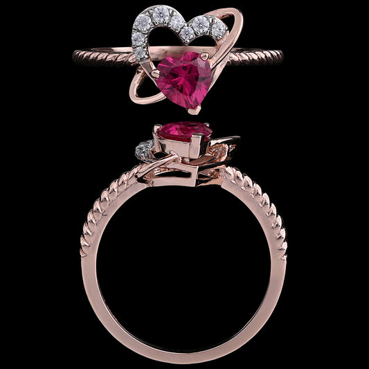 Heart-shaped ruby ring with diamond-accented open-heart design on a twisted rose gold band. Elegant and romantic fine jewelry by jnjbymadhuri.