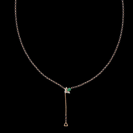 Elegant jnjbymadhuri mangalsutra set against a black background, featuring a delicate black bead chain accented with a striking emerald green stone centerpiece and a refined gold drop pendant, blending traditional symbolism with modern sophistication.