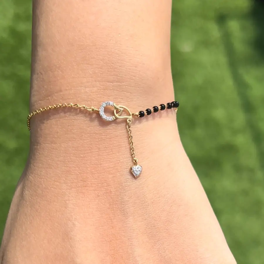 Elegant mangalsutra bracelet featuring a diamond-studded circular charm and heart drop, paired with classic black beads on a dual-tone gold chain. A signature fusion accessory by jnjbymadhuri.