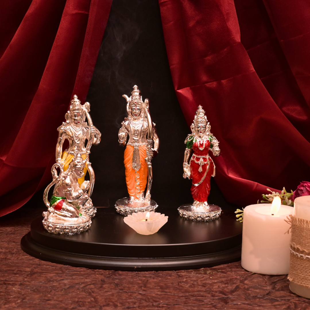 Three silver statues on a black platform with candles and red fabric in the background
