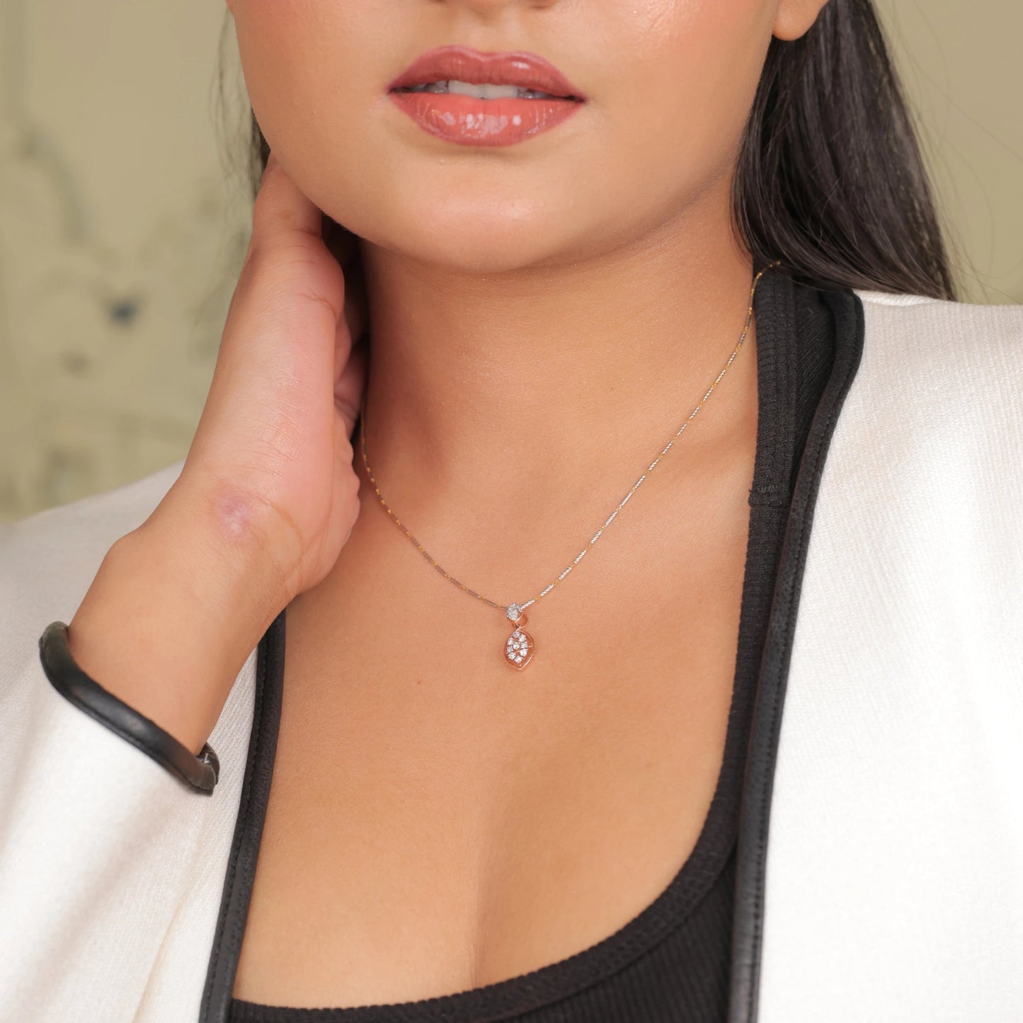Woman wearing a delicate marquise-shaped rose gold pendant necklace with diamond accents, styled with a black top and white blazer.