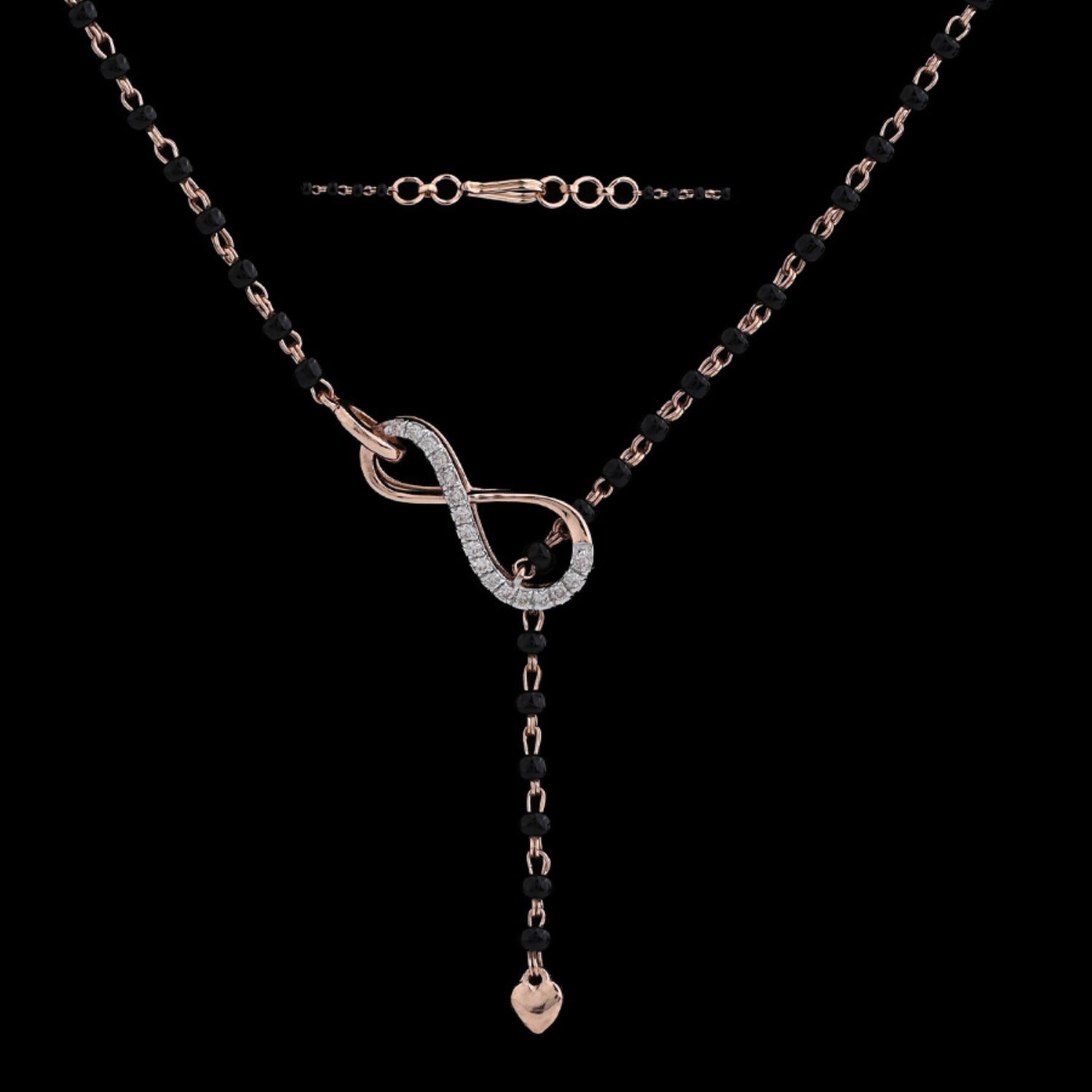This image presents a detailed view of the jnjbymadhuri infinity mangalsutra laid flat on a black background. The rose gold infinity centerpiece is partially studded with sparkling stones, and the single drop charm enhances its graceful design. The black beaded chain and adjustable clasp highlight the fusion of traditional and modern styling.