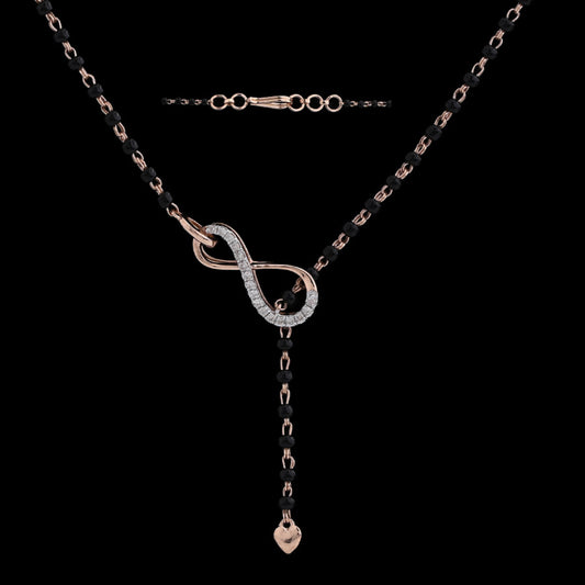This image presents a detailed view of the jnjbymadhuri infinity mangalsutra laid flat on a black background. The rose gold infinity centerpiece is partially studded with sparkling stones, and the single drop charm enhances its graceful design. The black beaded chain and adjustable clasp highlight the fusion of traditional and modern styling.