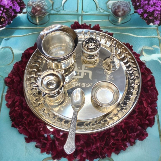 Silver pooja thali with utensils on a red floral mat against a blue background