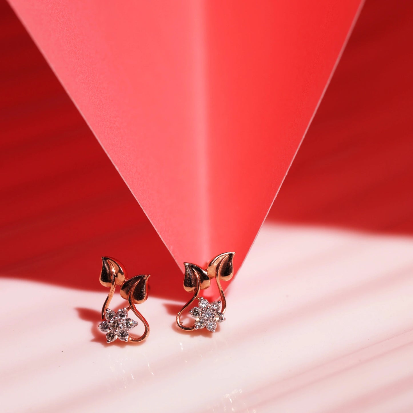 Elegant bow-shaped earrings from jnjbymaduri, featuring dazzling stones in a heart-shaped drop design, beautifully highlighted against a bold red and pink geometric backdrop.