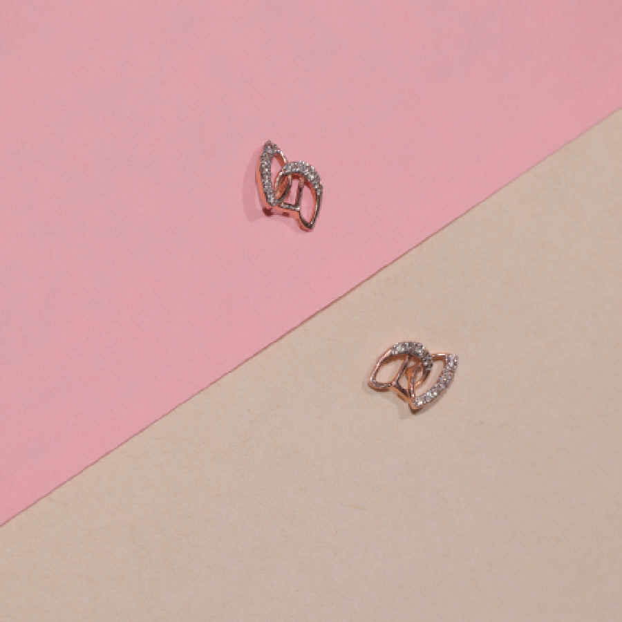 Delicate rose gold earrings with a leaf-inspired diamond design by jnjbymadhuri, styled against a pastel pink and beige backdrop for a soft, elegant presentation.