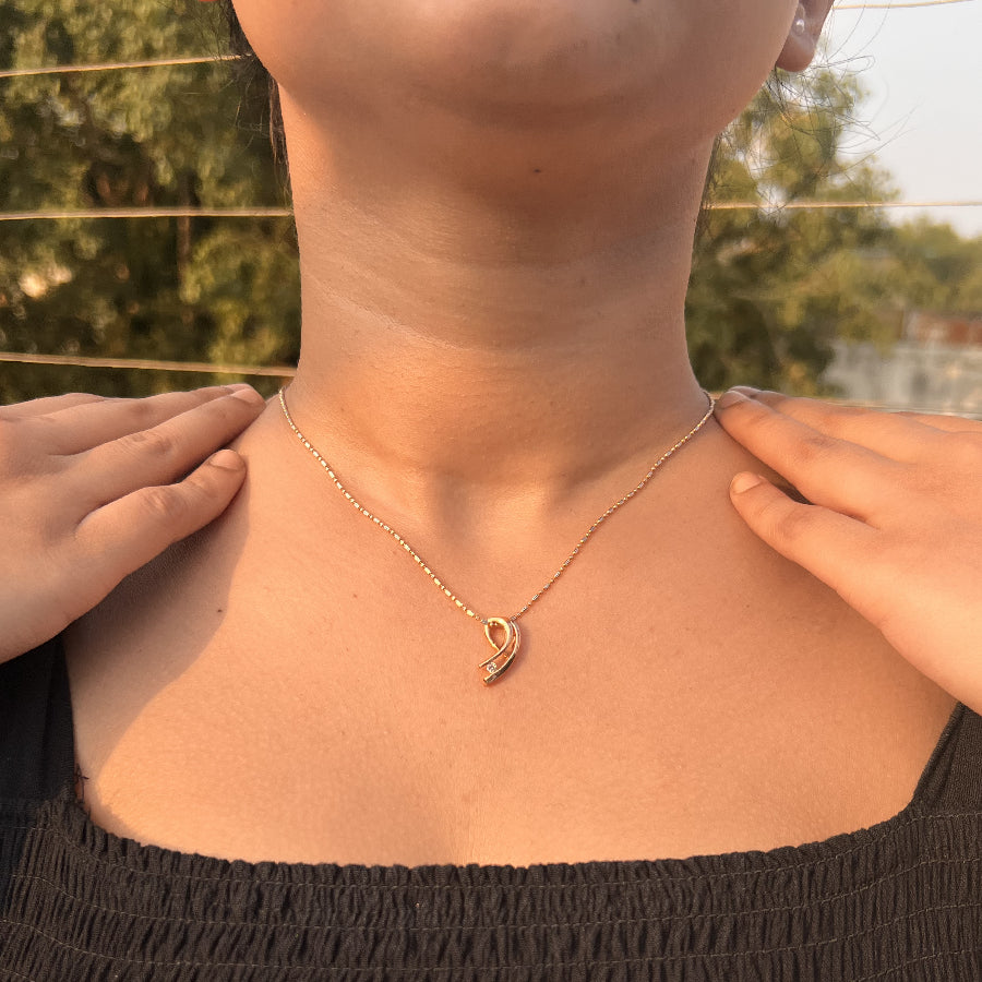Model wearing a delicate jnjbymadhuri rose gold necklace with a contemporary curved pendant featuring a small white stone, styled outdoors with a black textured off-shoulder top.