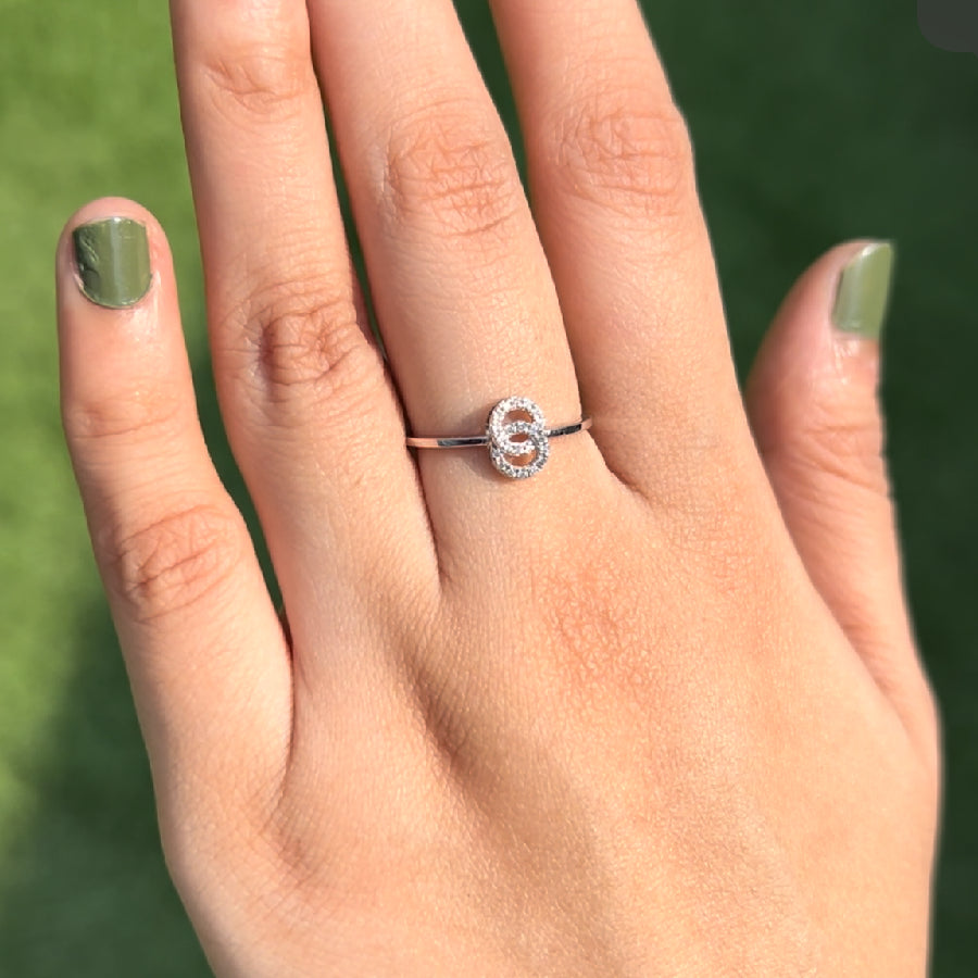 A dainty silver ring featuring a double-circle design adorned with tiny sparkling stones, elegantly worn on a hand with olive green nails, beautifully capturing the minimalistic charm and contemporary grace of jnjbymadhuri.