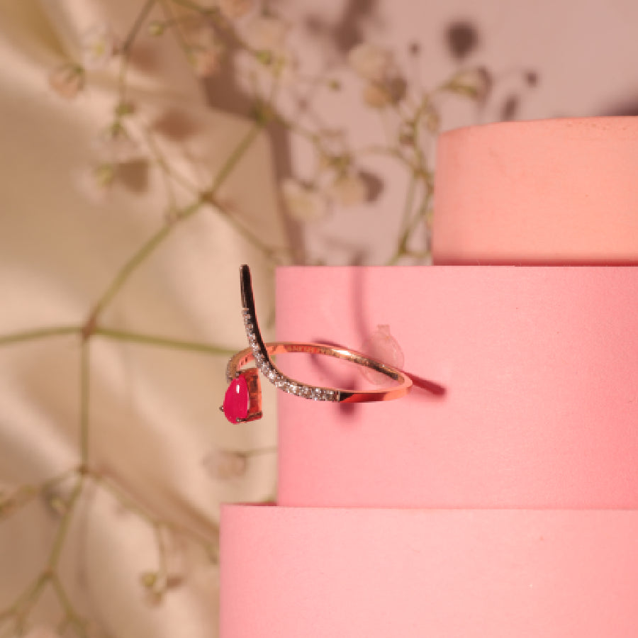 Heart-shaped ruby ring with a diamond-studded curved band set in rose gold, styled elegantly on pink spirals. A timeless piece by jnjbymadhuri.