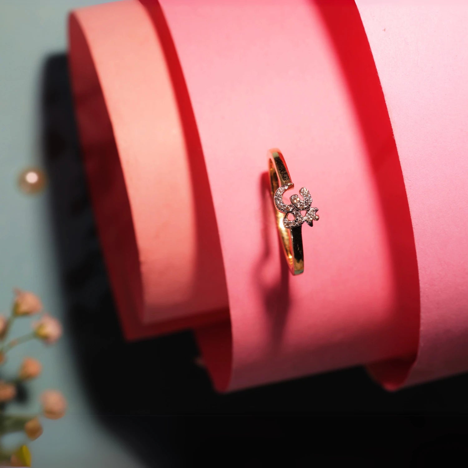 A dainty gold ring with a solitaire diamond centerpiece is elegantly displayed on soft pink paper curls, creating a romantic and graceful visual appeal, reflecting the timeless charm of jnjbymadhuri.
