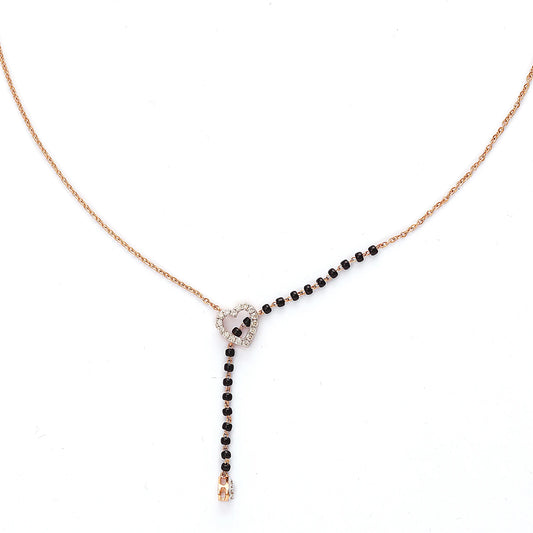 This image showcases a sleek heart-shaped mangalsutra design. It features a modern rose gold chain with a delicate black-beaded section flowing through a central, silver-tone heart charm. The heart is subtly adorned with sparkling stones, and a single drop at the end adds elegance. This piece blends contemporary aesthetics with traditional symbolism beautifully.