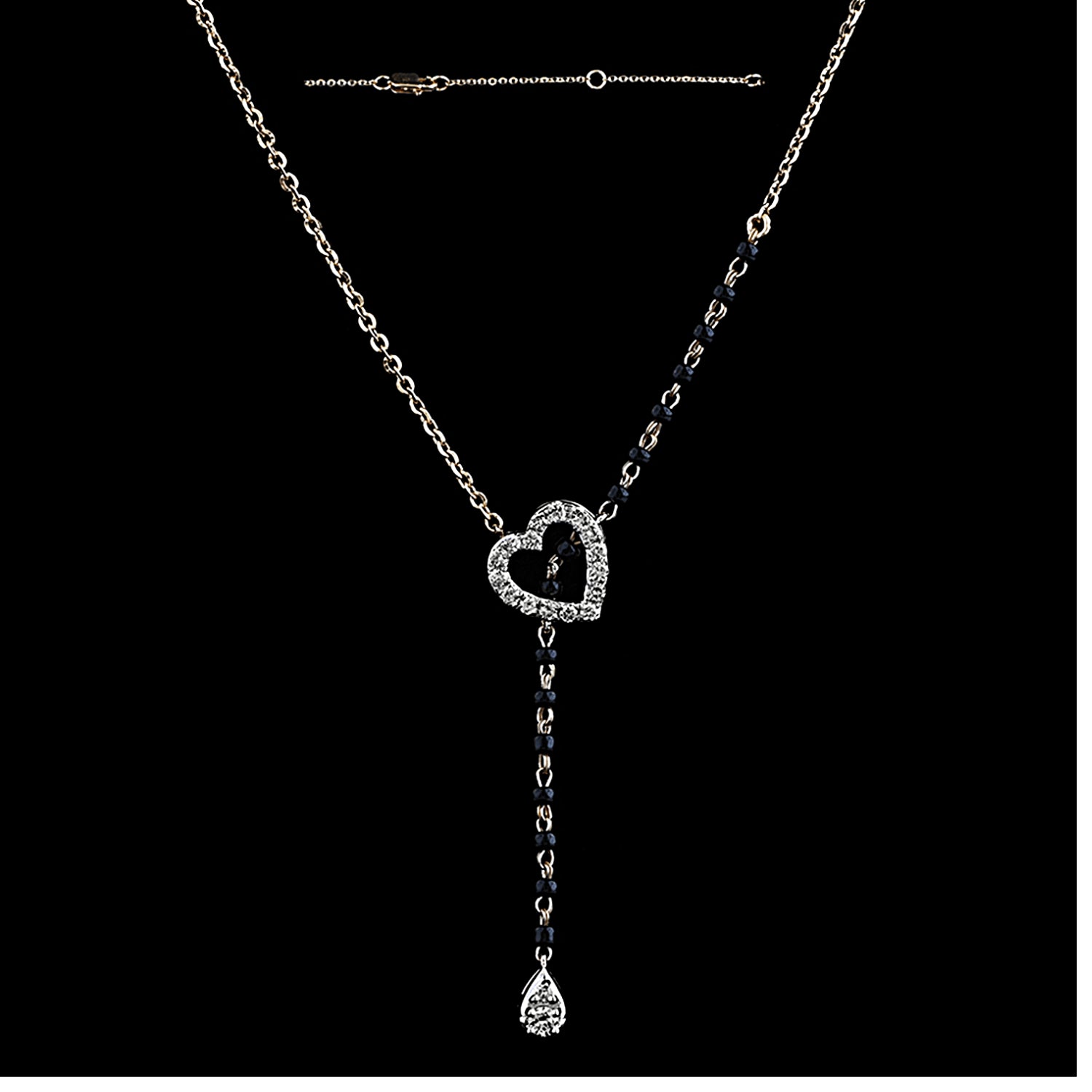 A stylish and elegant diamond heart mangalsutra by jnjbymadhuri, featuring a sparkling heart-shaped pendant encrusted with diamonds, complemented by a delicate drop-shaped diamond hanging below. The necklace combines a traditional black bead chain on one side with a sleek gold chain on the other, creating a modern, asymmetrical design perfect for contemporary Indian fashion.