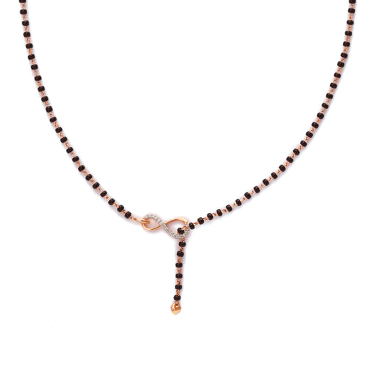 A minimal and elegant mangalsutra necklace from jnjbymadhuri, featuring a delicate black beaded chain with a central rose gold infinity-shaped motif, symbolizing eternal love, and a short vertical drop ending in a single gold bead, all showcased against a clean white background.
