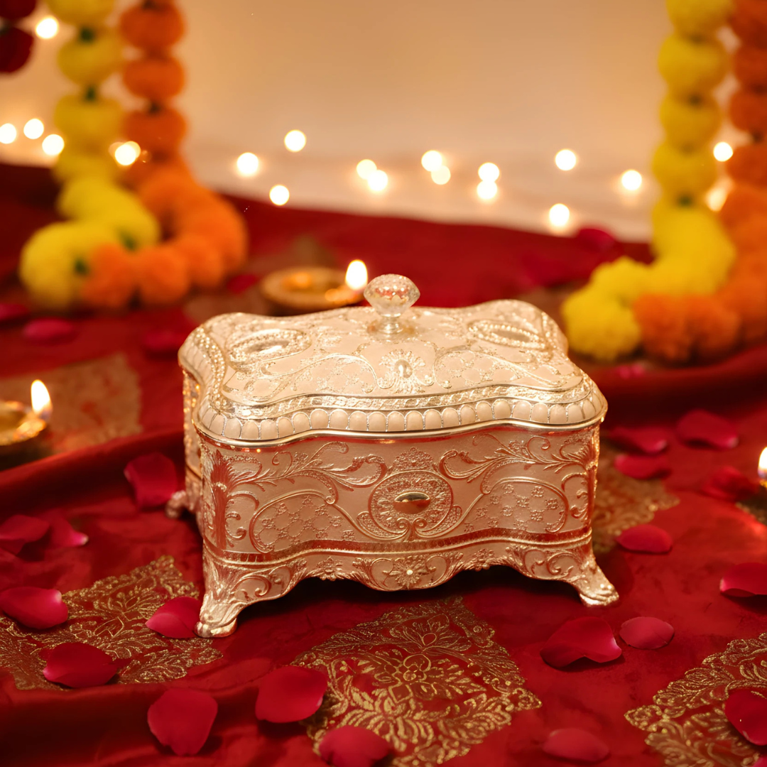 Decorative silver jewelry box on a red fabric background with floral arrangements and lights.