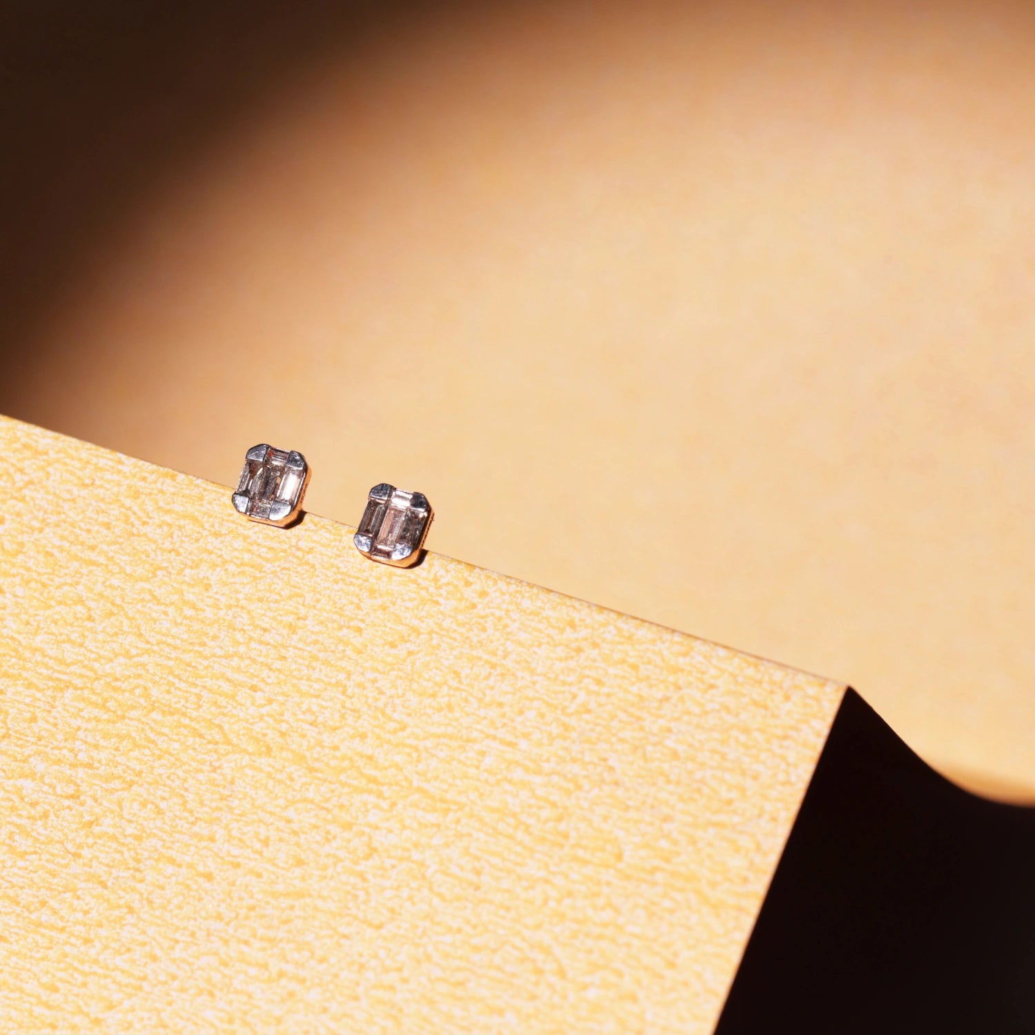 This photo showcases the same jnjbymaduri geometric rectangular stud earrings in a lifestyle setting. The minimal, reflective surface of the design pairs elegantly with the warm backdrop, highlighting their understated luxury—perfect for both daily wear and formal settings.
