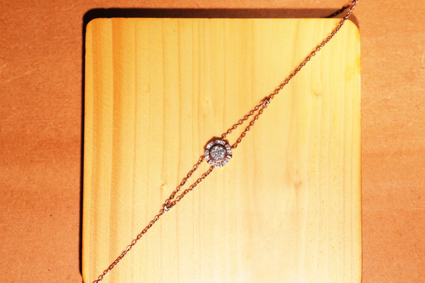 This image features the same rose gold bracelet by jnjbymadhuri, now displayed on a light wooden square base. The floral diamond motif remains the focal point, and the warm wood tones complement the metal’s rose hue, enhancing the bracelet’s elegance with a rustic yet refined presentation.
