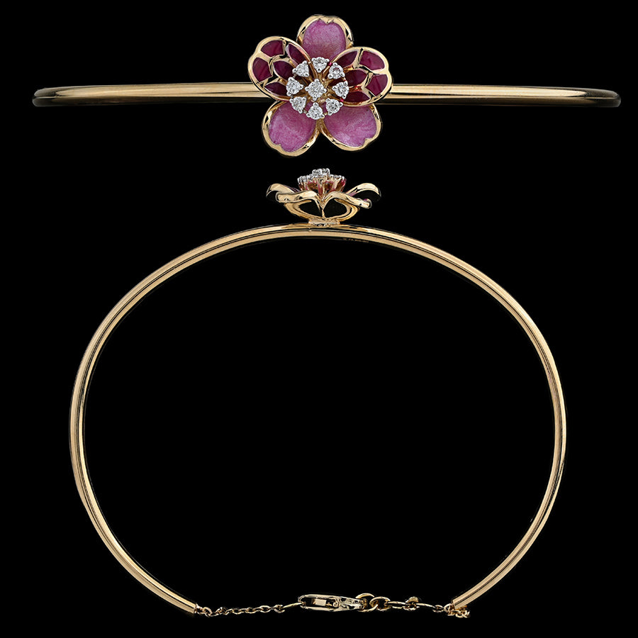 An exquisite gold bangle by jnjbymadhuri, featuring a beautifully crafted floral centerpiece with pink and deep red enamel petals and a sparkling diamond-studded core. The sleek, minimal band is secured with a delicate chain clasp, blending elegance with a feminine charm.
