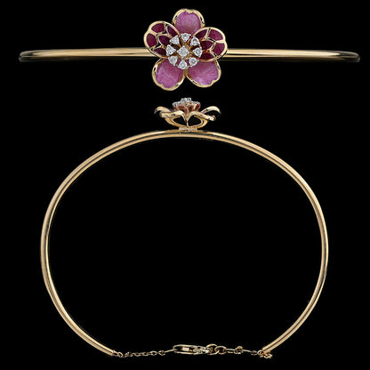 An exquisite gold bangle by jnjbymadhuri, featuring a beautifully crafted floral centerpiece with pink and deep red enamel petals and a sparkling diamond-studded core. The sleek, minimal band is secured with a delicate chain clasp, blending elegance with a feminine charm.
