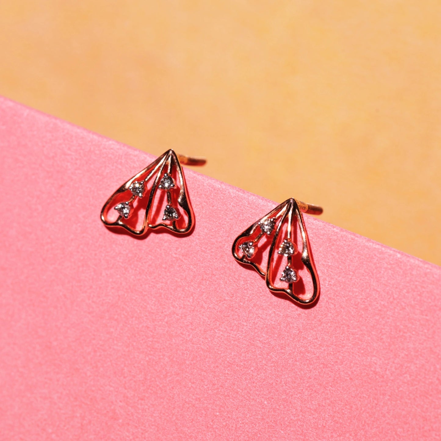 This styled photo beautifully highlights the triangular rose gold earrings by jnjbymadhuri, emphasizing their sleek openwork design and the delicate sparkle of the embedded diamonds. The warm tones and minimalist aesthetic make them perfect for both casual and formal wear.
