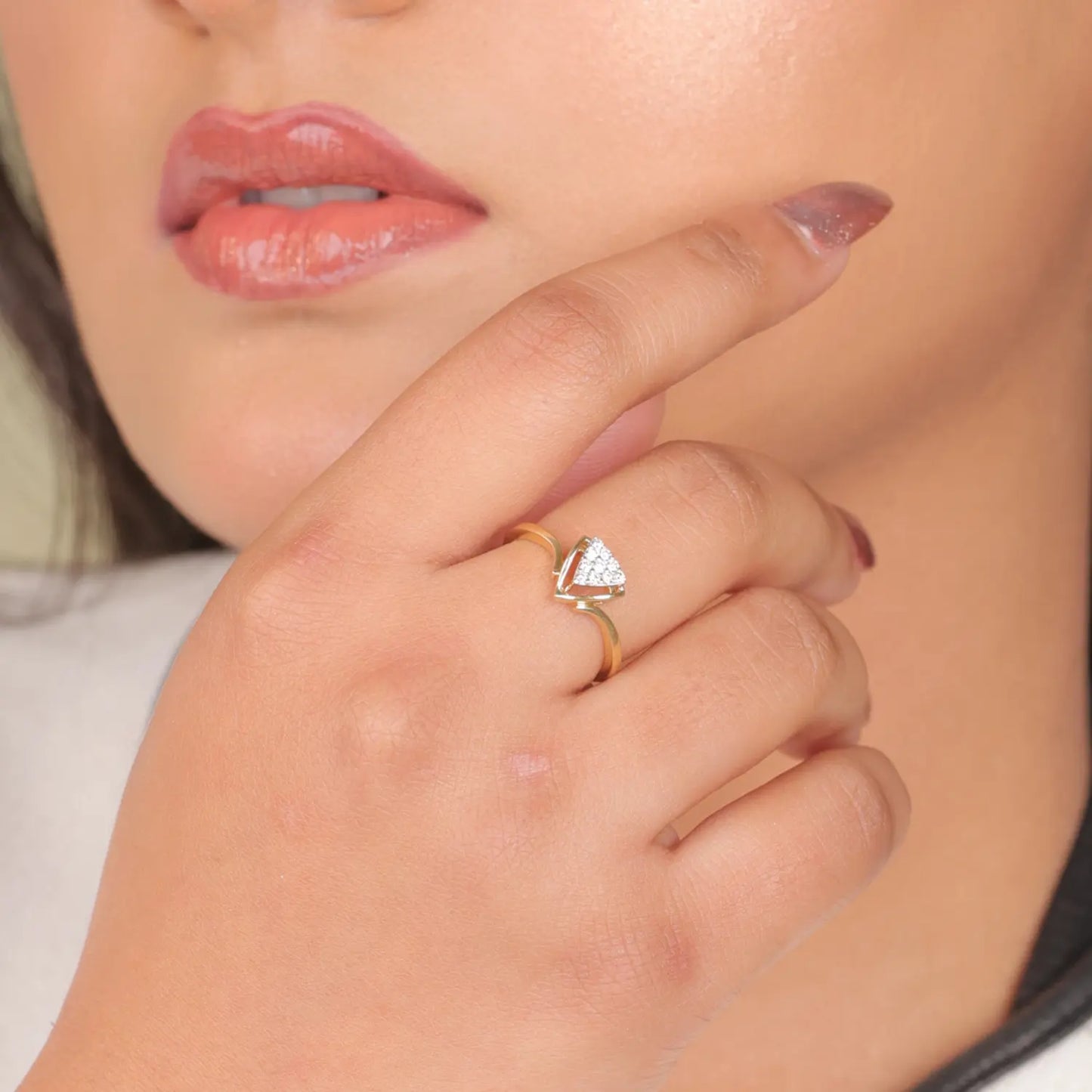 A woman wearing a gold ring with a heart-shaped white stone on her ring finger, showcasing the elegant and minimalistic jewelry piece from jnjbymadhuri; the ring complements her manicured nails and neutral outfit, emphasizing the brand's refined and contemporary style.
