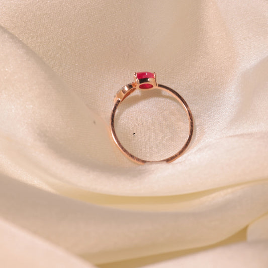 Rose gold ring with a single red gemstone centerpiece, elegantly displayed on soft ivory satin fabric, by jnjbymadhuri.