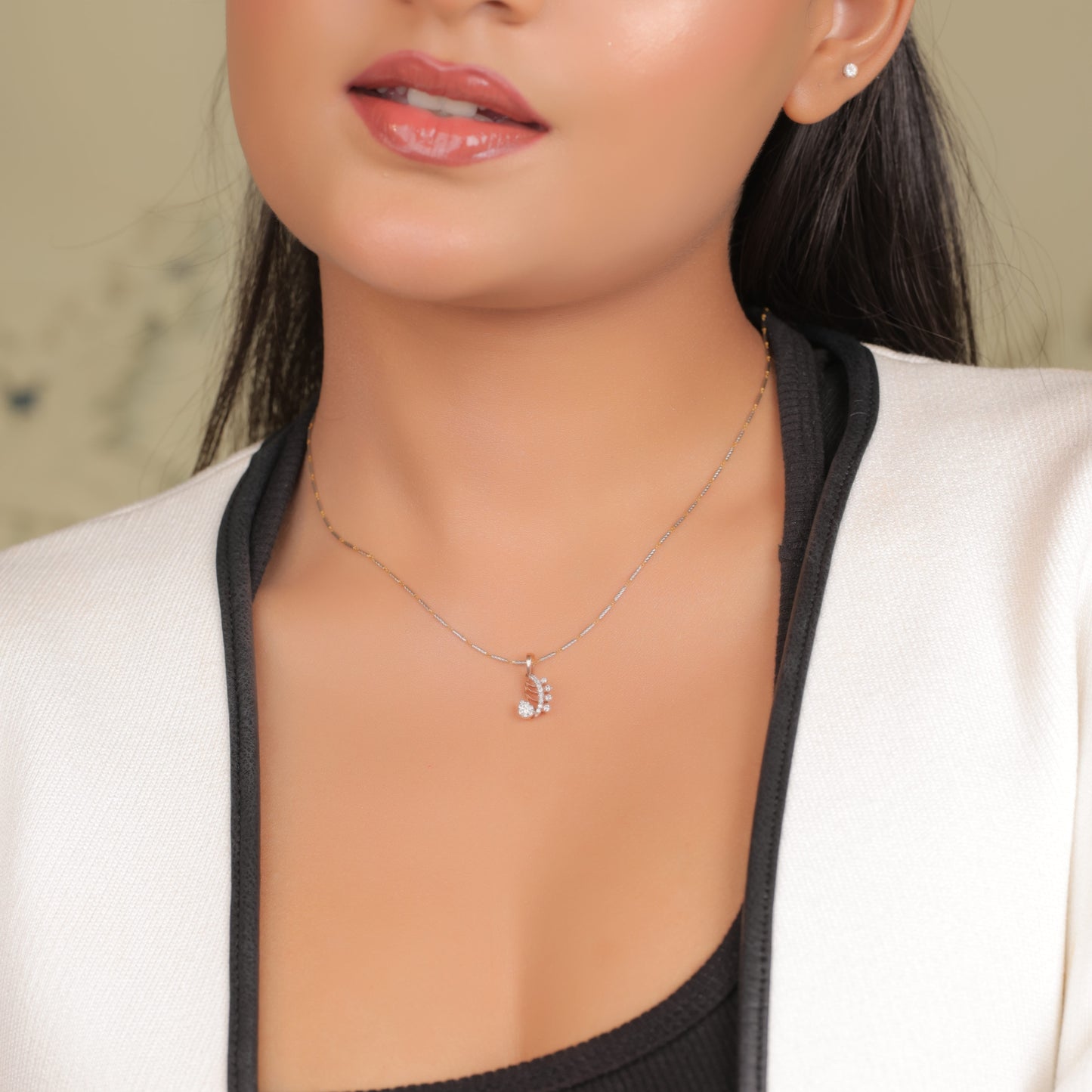 Model wearing a delicate rose gold paisley-shaped pendant necklace by jnjbymadhuri, featuring embedded white stones, styled with a white blazer and black inner top.
