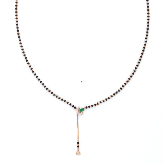 A minimalistic and elegant mangalsutra by jnjbymadhuri, showcasing a classic black bead chain with a sleek gold drop pendant. The centerpiece features a subtle green gemstone accent, adding a touch of color and sophistication to the design. Perfect for modern brides who appreciate understated traditional jewelry with a contemporary twist.
