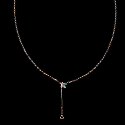 Elegant jnjbymadhuri mangalsutra set against a black background, featuring a delicate black bead chain accented with a striking emerald green stone centerpiece and a refined gold drop pendant, blending traditional symbolism with modern sophistication.
