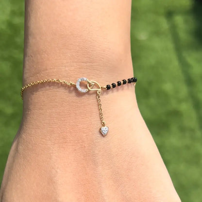 Elegant mangalsutra bracelet featuring a diamond-studded circular charm and heart drop, paired with classic black beads on a dual-tone gold chain. A signature fusion accessory by jnjbymadhuri.
