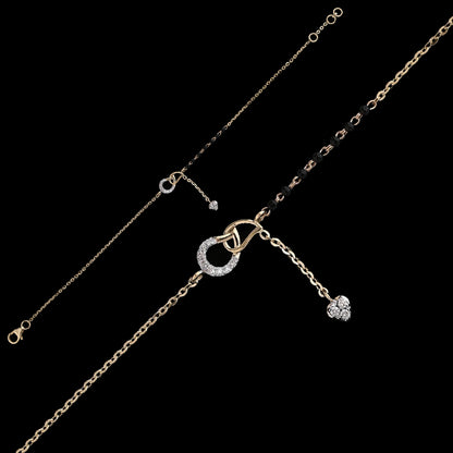 Contemporary mangalsutra bracelet in dual-tone gold, featuring a circular diamond-studded charm with a dangling heart pendant and traditional black bead detailing. A chic fusion piece by jnjbymadhuri.
