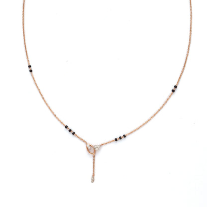 Minimalist mangalsutra with a delicate rose gold chain, accented by small black beads and featuring a central knot-like pendant with a vertical drop element, displayed on a white background.
