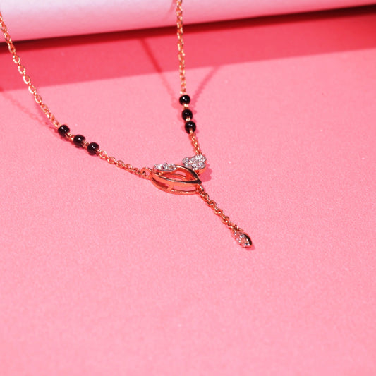 Elegant mangalsutra with a rose gold chain and black bead accents, featuring a central knot-style pendant with a vertical dangling drop, displayed on a vibrant pink background.
