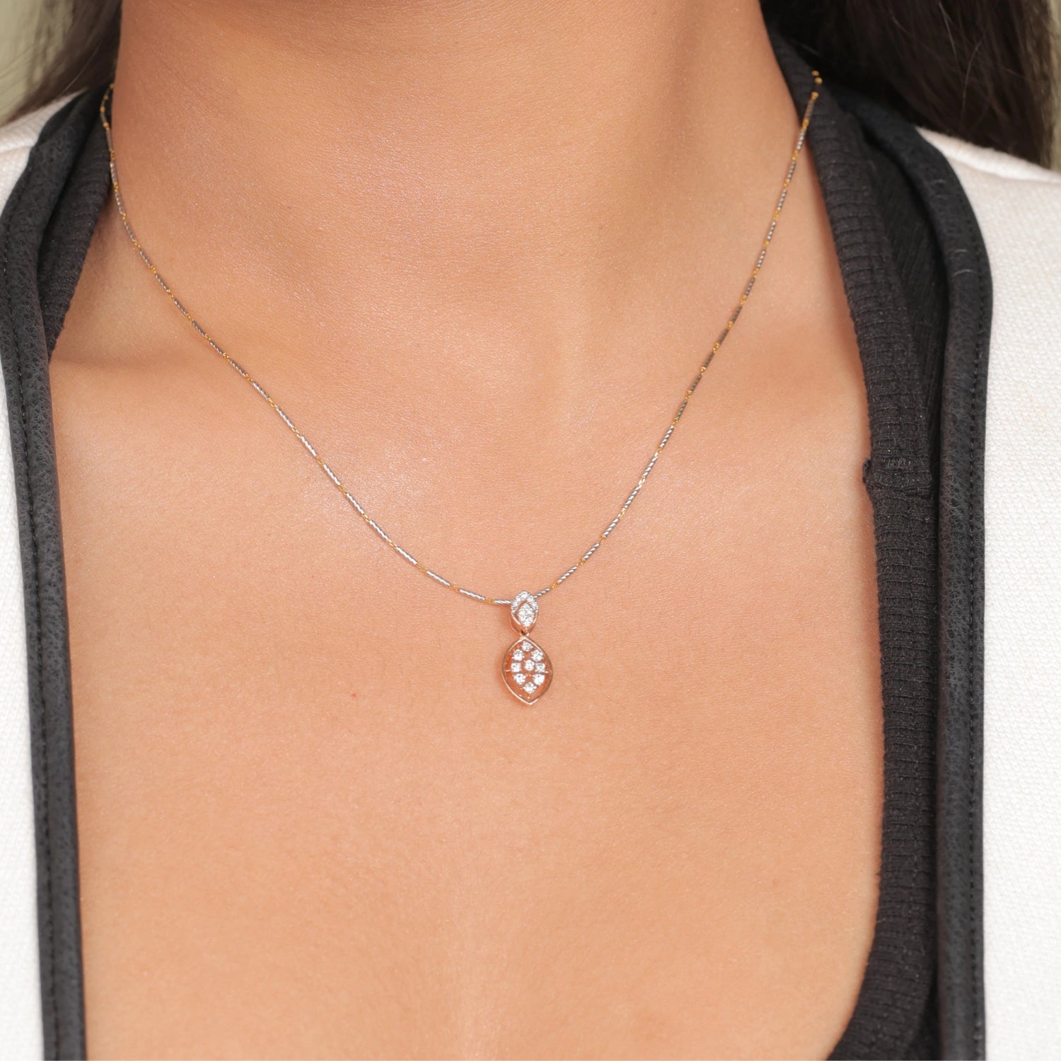 Close-up of a woman wearing a rose gold marquise-shaped diamond pendant necklace on a delicate chain, paired with a black top and white blazer.
