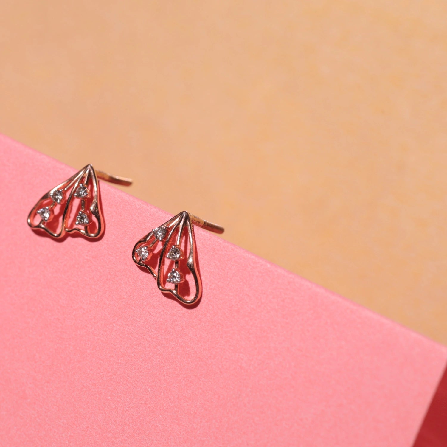 This styled photo beautifully highlights the triangular rose gold earrings by jnjbymadhuri, emphasizing their sleek openwork design and the delicate sparkle of the embedded diamonds. The warm tones and minimalist aesthetic make them perfect for both casual and formal wear.
