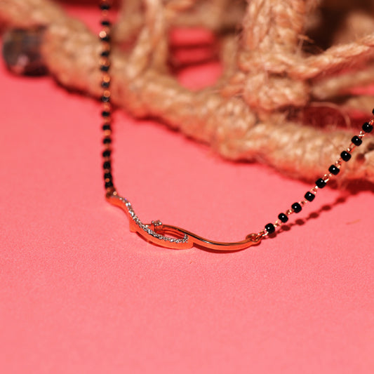 Elegant black beaded mangalsutra with a curved gold and diamond pendant, artistically placed on a coral pink background with natural twine in the backdrop.
