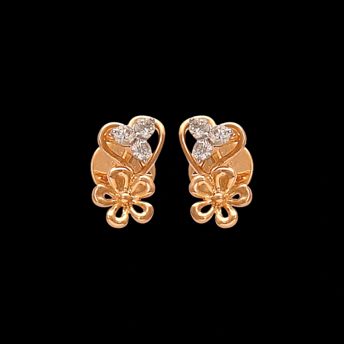 These graceful gold stud earrings by jnjbymadhuri feature a romantic heart-shaped design accented with delicate floral detailing and shimmering diamonds, blending charm and elegance in a timeless accessory.
