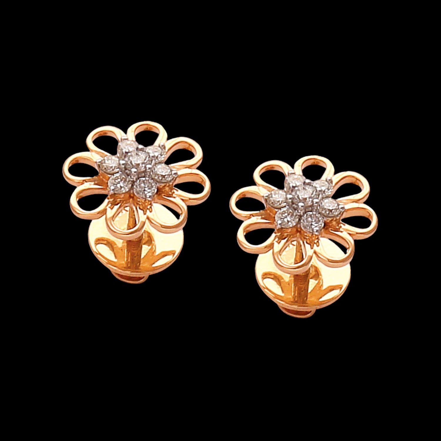 A pair of radiant floral stud earrings by jnjbymadhuri, crafted in gold with petal-like open loops and a sparkling cluster of diamonds at the center, exuding timeless elegance against a bold black background.
