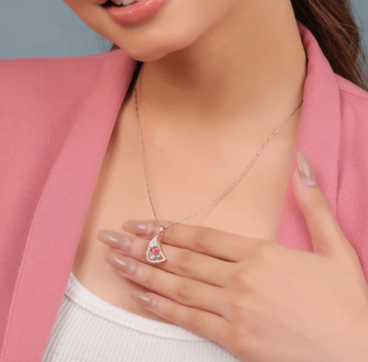Model showcasing a stylish jnjbymadhuri pendant necklace featuring a rose gold crescent-shaped charm adorned with dazzling stones and colorful gems, elegantly paired with a delicate chain and worn over a white top and pink blazer for a chic, sophisticated look.
