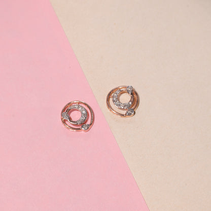 "Rose gold circular earrings with diamond accents arranged on a diagonally split pink and beige background, from jnjbymadhuri."
