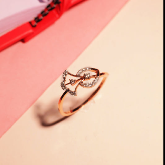 Elegant rose gold ring by jnjbymadhuri with a double-leaf design set with sparkling white stones, placed on a soft peach and pink background beside a red-bound notebook.

