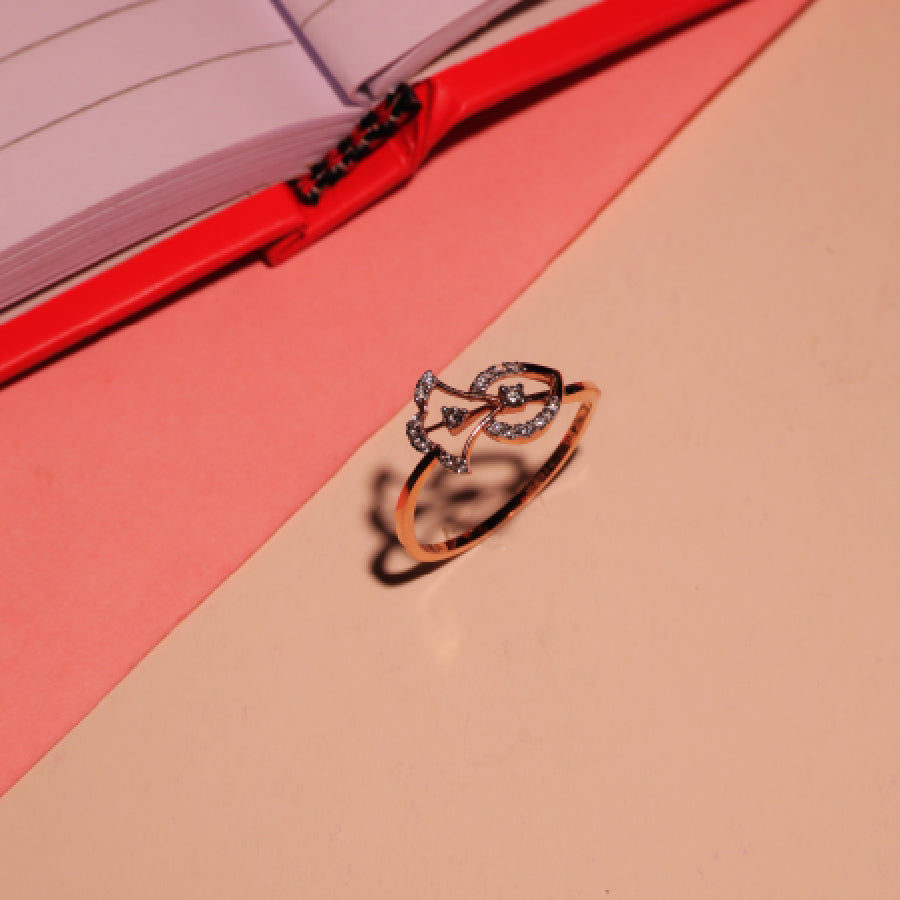 Rose gold designer ring by jnjbymadhuri featuring a delicate dual-leaf motif adorned with diamonds, resting on a peach surface beside an open red notebook with a pink sheet beneath.
