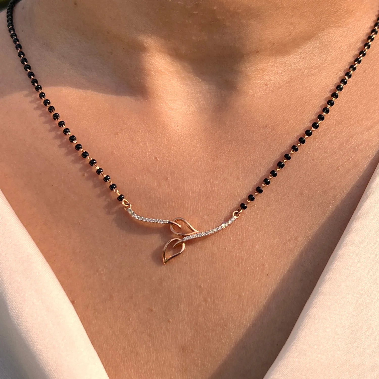 Close-up view of a jnjbymadhuri mangalsutra, showcasing its delicate black beaded chain and modern twin-leaf gold pendant design, worn gracefully on the neck for a timeless, elegant look.
