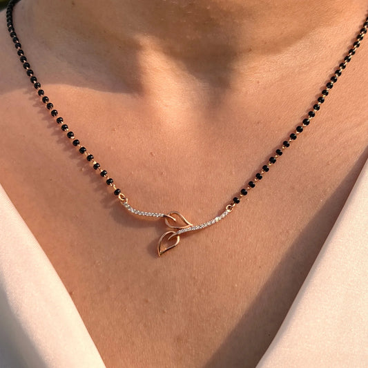 Close-up view of a jnjbymadhuri mangalsutra, showcasing its delicate black beaded chain and modern twin-leaf gold pendant design, worn gracefully on the neck for a timeless, elegant look.
